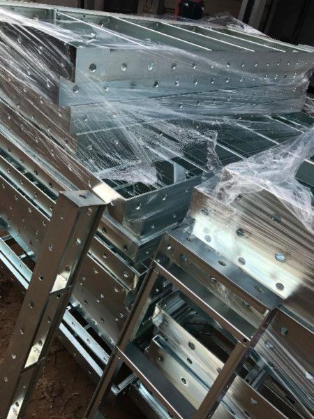 Stos ocynkowanych, metalowych konstrukcji ramowych z otworami, zabezpieczonych folią stretch.