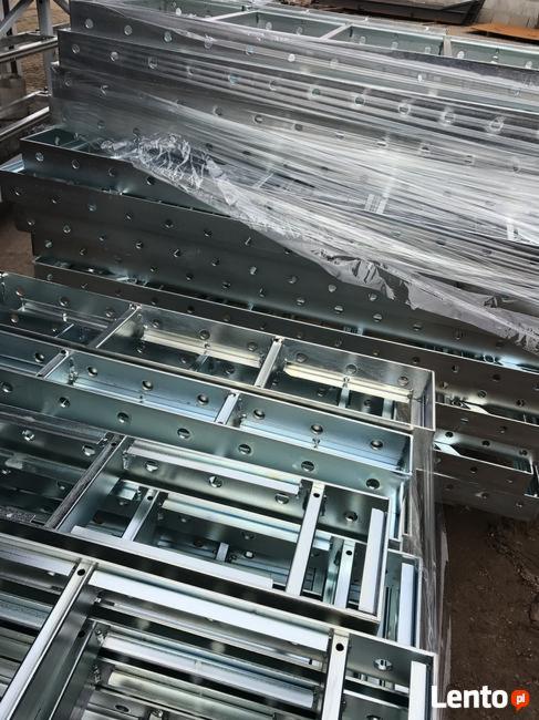 Stos metalowych szalunków budowlanych, częściowo owiniętych folią, przygotowanych do transportu lub magazynowania.