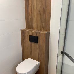 Dariusz Dybowski Paxbud Professional - Nowoczesna łazienka po remoncie: podwieszana toaleta z drewnopodobną obudową i czarnym przyciskiem, białe, poziome płytki na ścianach, kabina prysznicowa z czarnymi ramami.