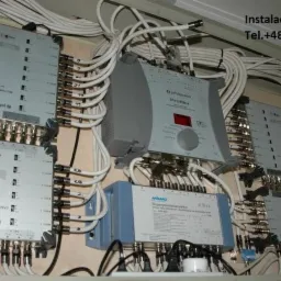 Rozdzielnice sygnału TV-SAT z podłączonymi kablami koncentrycznymi w szafce instalacyjnej, widoczne urządzenia marki Johansson i Ankaro.