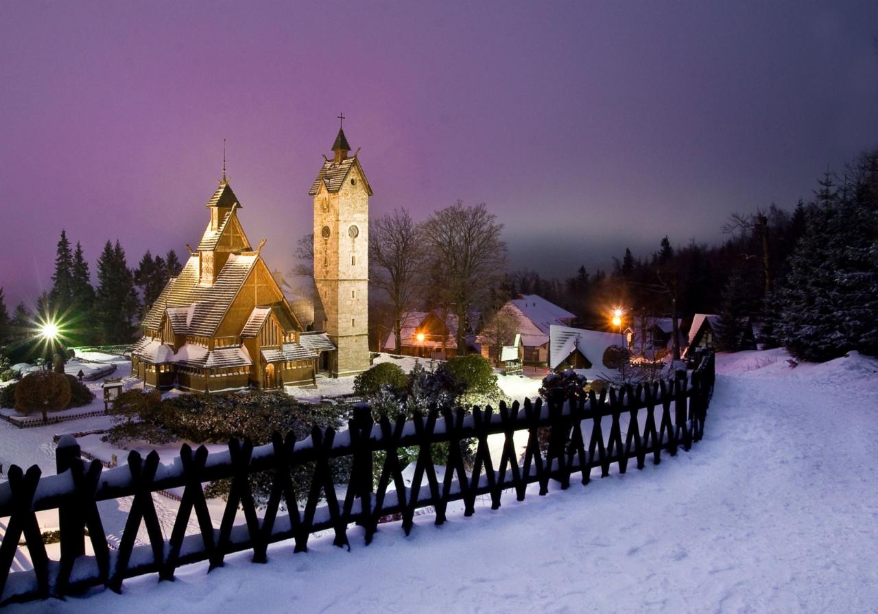 Karpacz, Kościół Wang w zimowej scenerii, oświetlony nocą, widok zza drewnianego płotu.
