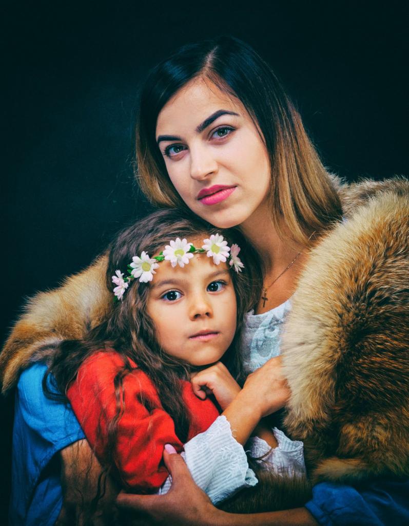 Portret matki i córki w stylizowanych strojach z futrzanym okryciem, dziewczynka ma wianek z białych kwiatów.