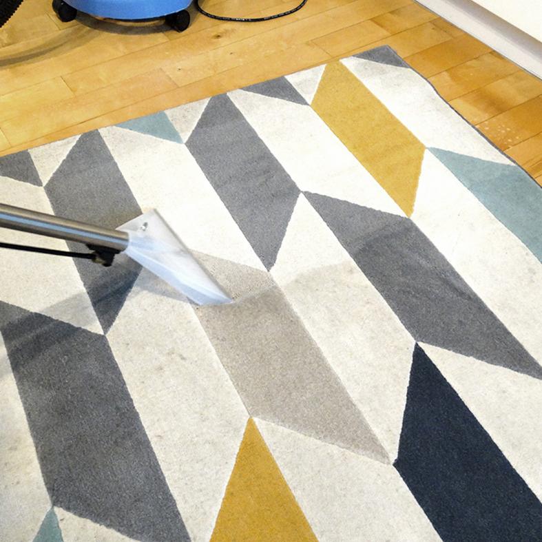 Czyszczenie geometrycznego dywanu odkurzaczem piorącym, widoczne ślady wilgoci na czyszczonej powierzchni.