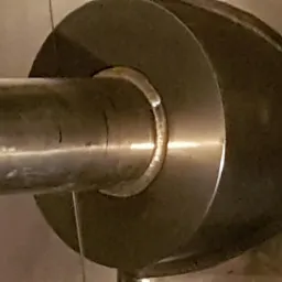 Metalowy pręt połączony z okrągłą tarczą, widoczne ślady łączenia i obróbki.