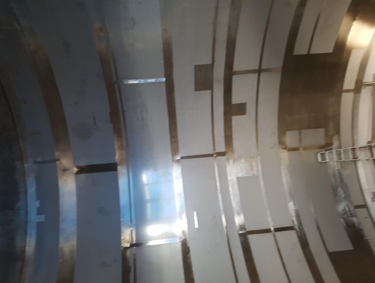 Wnętrze metalowej konstrukcji o zakrzywionym kształcie, z widocznymi spawami i elementami montażowymi, oświetlone z góry.