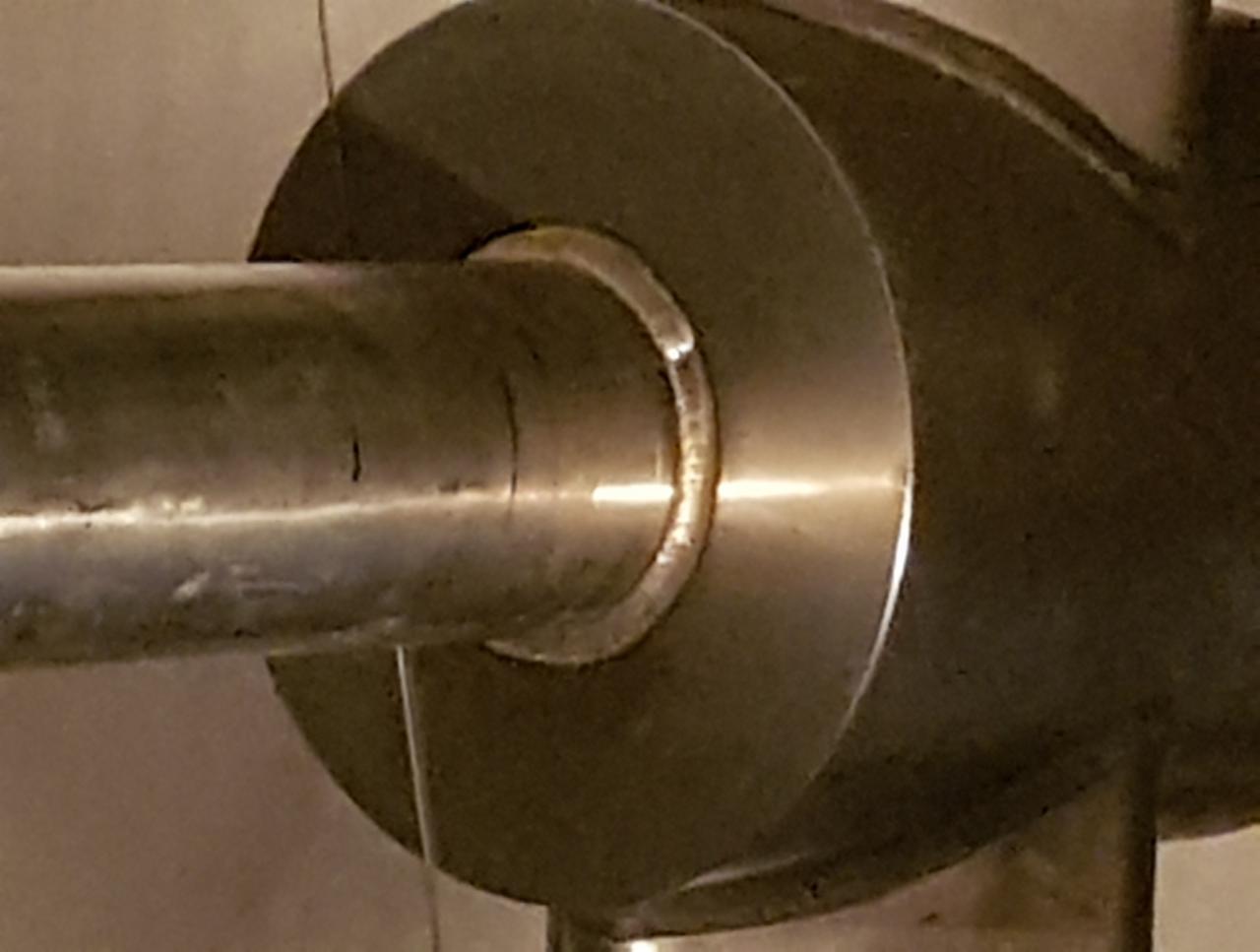 Metalowy pręt połączony z okrągłą tarczą, widoczne ślady łączenia i obróbki.