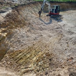 BET GROUNDWORKS SPÓŁKA Z OGRANICZONĄ ODPOWIEDZIALNOŚCIĄ - Mini koparka Takeuchi TB250 w trakcie prac ziemnych, widoczny wykop w jasnej, kamienistej glebie. Ślady opon i łyżki koparki na powierzchni.