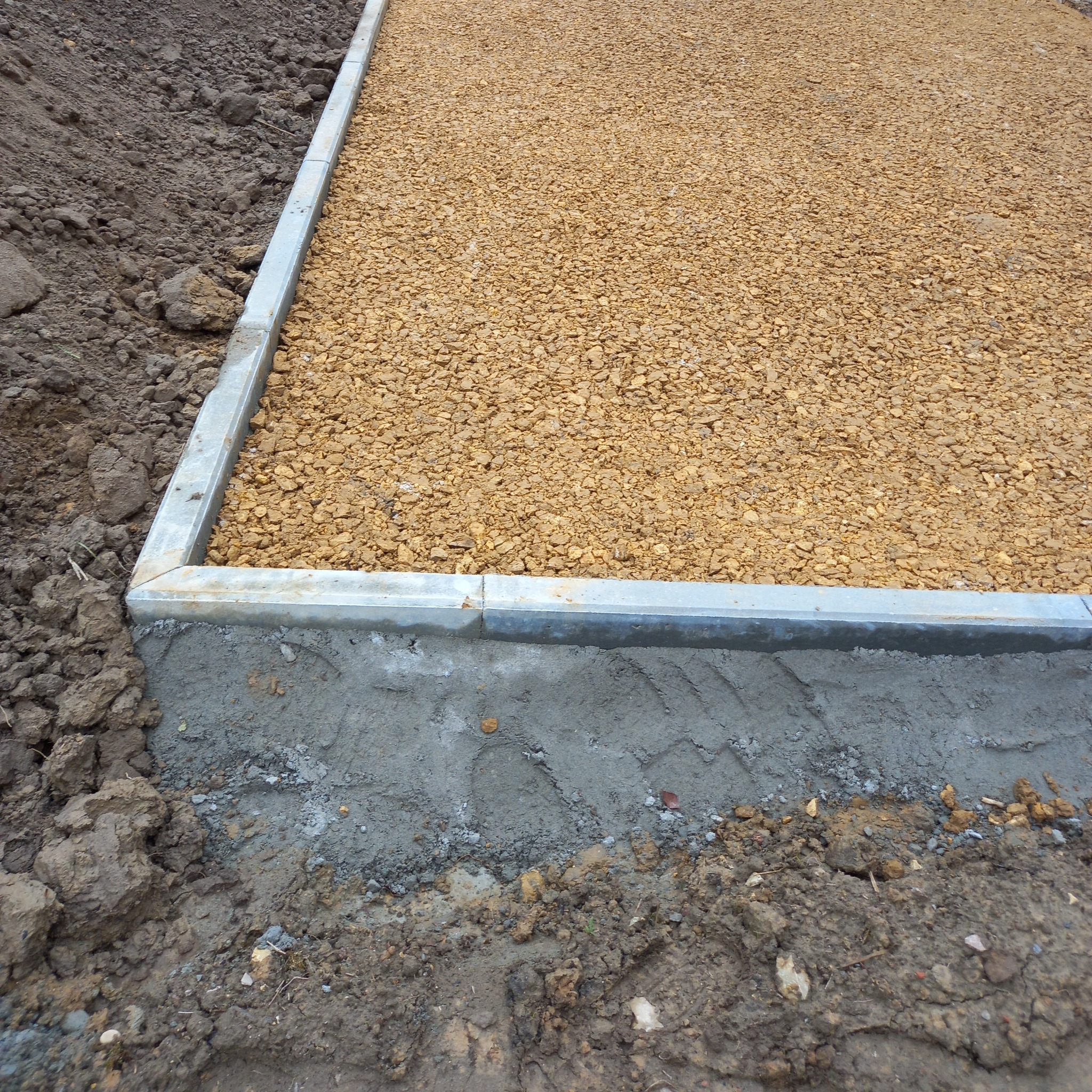 Utwardzona droga z obrzeżami w Trzebini. Żwir równomiernie rozłożony, obrzeża betonowe i metalowe. Etap prac ziemnych, widoczna gleba.