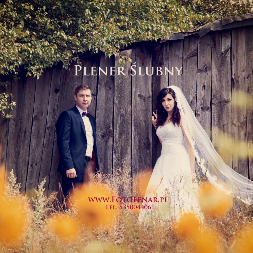 Para młoda w plenerze pozuje przy starej drewnianej chacie porośniętej bluszczem, z pomarańczowymi kwiatami na pierwszym planie.