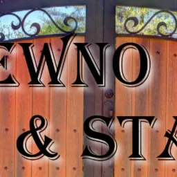 Dwuskrzydłowa brama z drewnianym wypełnieniem i metalową, ozdobną górną częścią, widoczne śruby mocujące drewno, zamek po lewej stronie, w tle zieleń i fragment budynku.