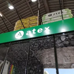 Ekspozycja w punkcie sprzedaży prezentująca różne rodzaje węgla i ekogroszku w przezroczystych pojemnikach pod zielonym szyldem firmy Atex i paletami worków na górze.