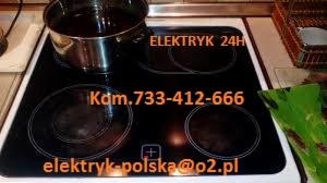 Czarna płyta indukcyjna z czterema polami grzejnymi, na jednym z nich stoi garnek. Widoczne dane kontaktowe elektryka. Ujęcie z góry, w tle blat kuchenny.