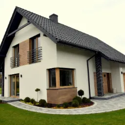 Nowoczesny dom jednorodzinny z białymi ścianami, czarnym dachem i drewnianymi akcentami okiennymi, otoczony zadbanym trawnikiem i ścieżką z kostki brukowej.