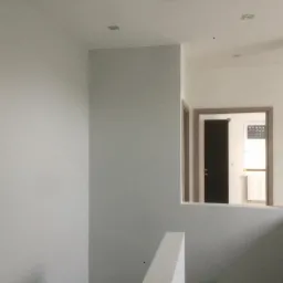 Świeżo pomalowane, jasnoszare ściany klatki schodowej z widokiem na drzwi i okno w głębi.