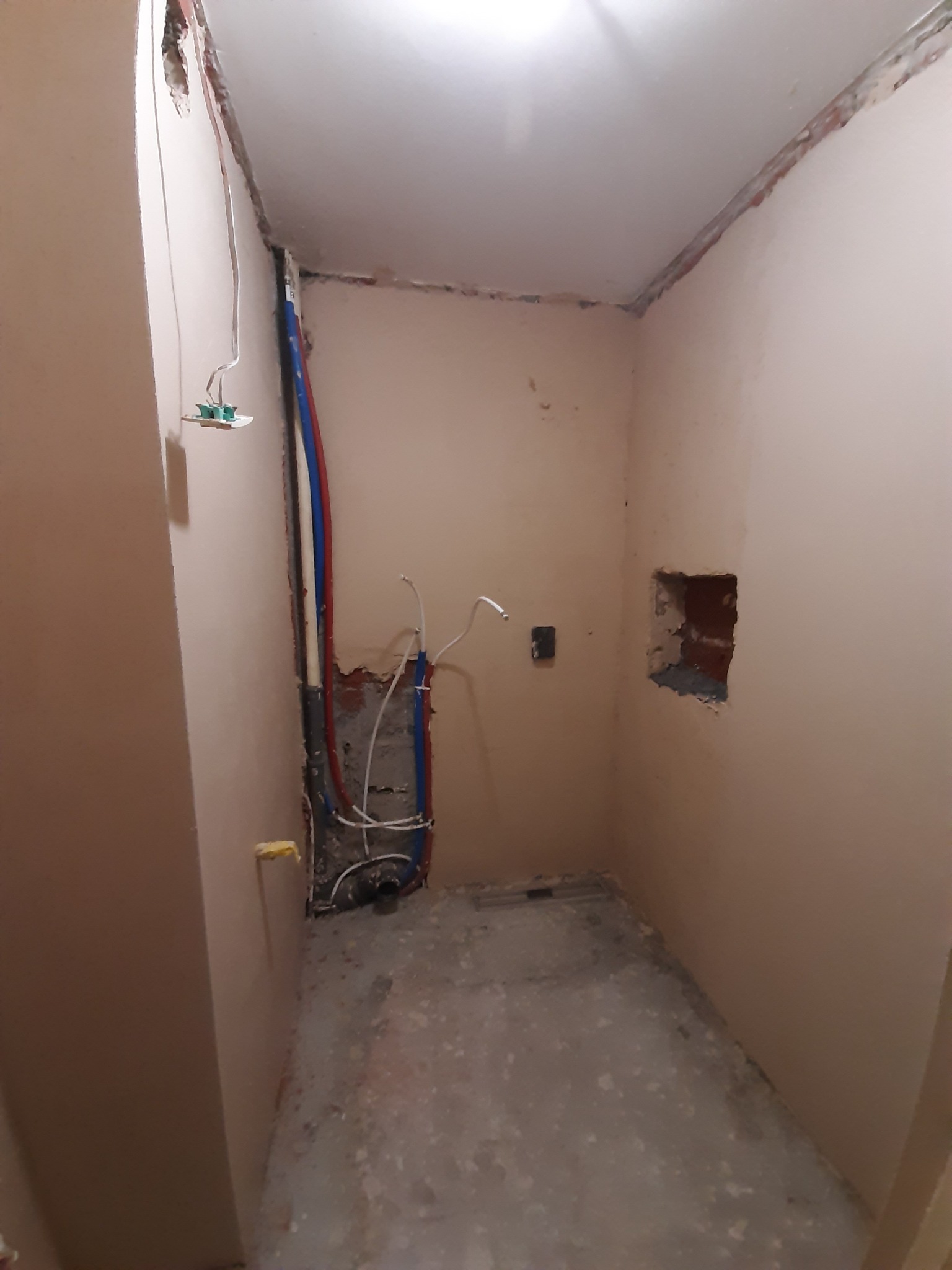 Łazienka w trakcie remontu: widoczne instalacje wodne i elektryczne w ścianach, surowy beton na podłodze, ściany przygotowane pod gładzie.