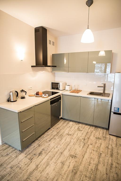 Nowoczesna kuchnia z szarymi, błyszczącymi frontami szafek, czarnym okapem, drewnopodobną podłogą i owocami na blacie.