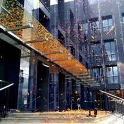 Nowoczesny budynek biurowy z ciemną elewacją i przeszklonym wejściem, obsypany konfetti podczas uroczystego otwarcia.