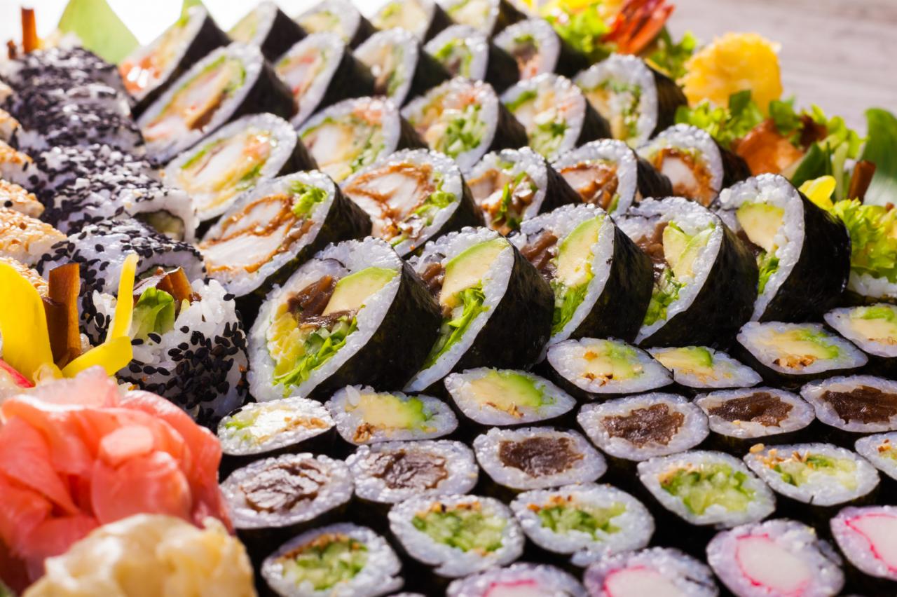 Bogaty wybór sushi na tacy: rolki z awokado, tempurą, warzywami i sezamem, udekorowane imbirem i zielenią.