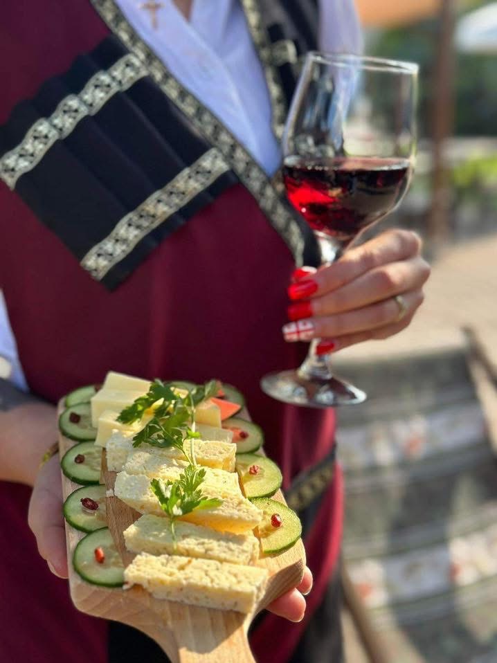 Deska serów z ogórkiem i kieliszek czerwonego wina w ręku osoby w tradycyjnym stroju, catering w Warszawie.