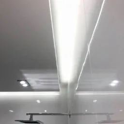 Nowoczesna kabina prysznicowa z białymi płytkami, oświetleniem LED w suficie i deszczownicą o kwadratowym kształcie.