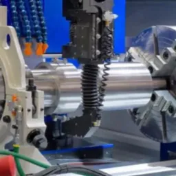 Srebrny wałek metalowy mocowany w uchwycie tokarskim, obrabiany przez frezarkę CNC z chłodziwem, widoczne przewody i elementy sterujące maszyny.