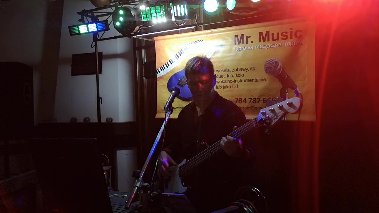 Basista grający na scenie z oświetleniem estradowym i banerem reklamowym z ofertą oprawy muzycznej imprez w tle.