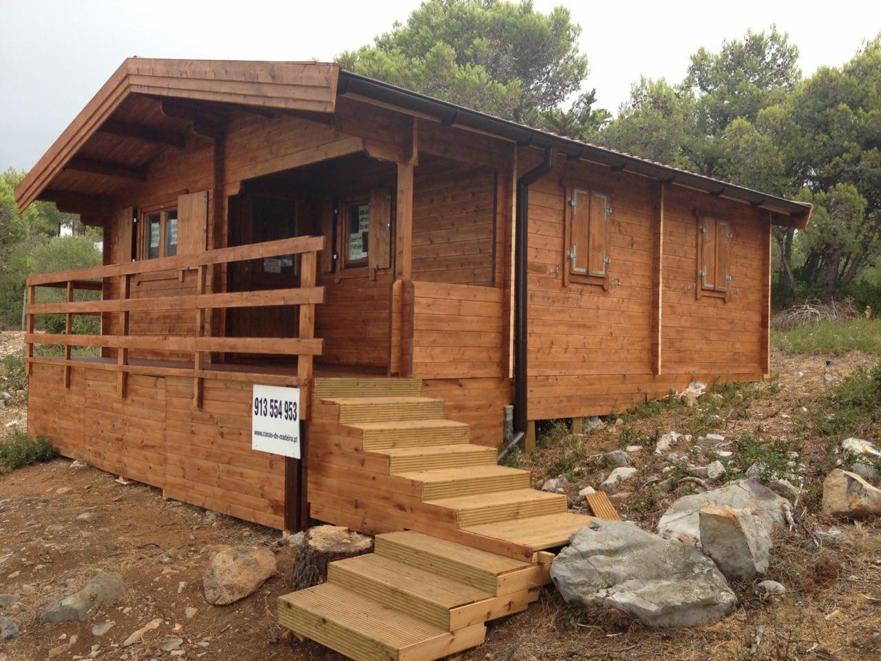 Gotowy, parterowy budynek z drewna, z tarasem i schodami wejściowymi, położony na nierównym terenie z kamieniami.