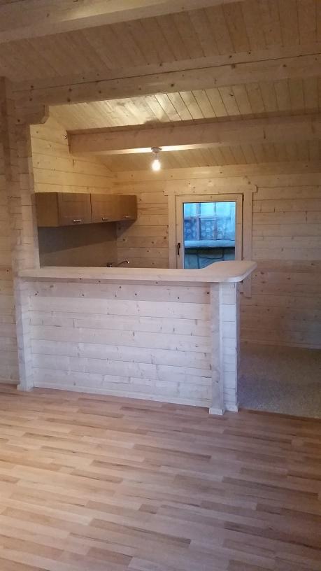 Wnętrze domu z bali z drewnianym barem, szafkami kuchennymi i widoczną strukturą drewna na ścianach i suficie.