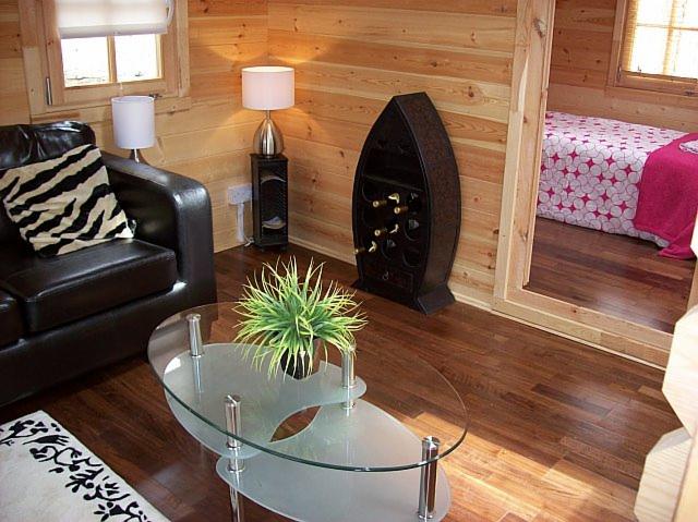 Wnętrze domku z drewnianymi ścianami, z czarną skórzaną sofą z poduszką w zebrę, szklanym stolikiem kawowym i regałem na wino w kształcie łodzi.