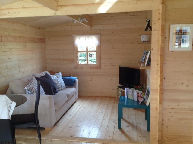 Wnętrze wykończonego jasnego pomieszczenia z drewnianych bali, z sofą, stolikiem i telewizorem, oświetlone naturalnym światłem z okna.