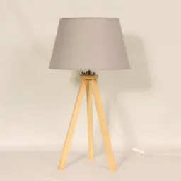 Lampa stołowa z szarym abażurem i drewnianym trójnożnym stelażem na białym tle.