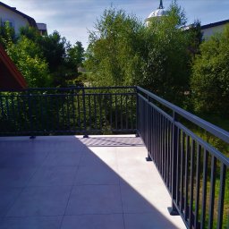 Hot Spaw SM Sebastian Moździerz - Nowoczesna, grafitowa balustrada balkonowa z pionowymi szczebelkami w Dąbrowie Tarnowskiej, z widokiem na zieleń i fragment zabudowań w tle.