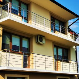 Hot Spaw SM Sebastian Moździerz - Dwupiętrowy dom z balkonami zabezpieczonymi nowoczesnymi, poziomymi balustradami ze stali nierdzewnej, z anteną satelitarną na górnym balkonie.