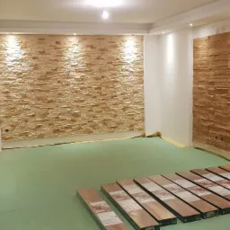 Salon w trakcie prac: ściana wyłożona dekoracyjnym kamieniem, druga ściana z drewnianą okładziną, na podłodze rozłożona zielona folia i paczki paneli podłogowych.