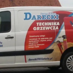 Biały samochód dostawczy z reklamą firmy Darecki Technika Grzewcza, prezentujący grafikę kotła grzewczego, adres firmy w Sidzinie i numer telefonu.