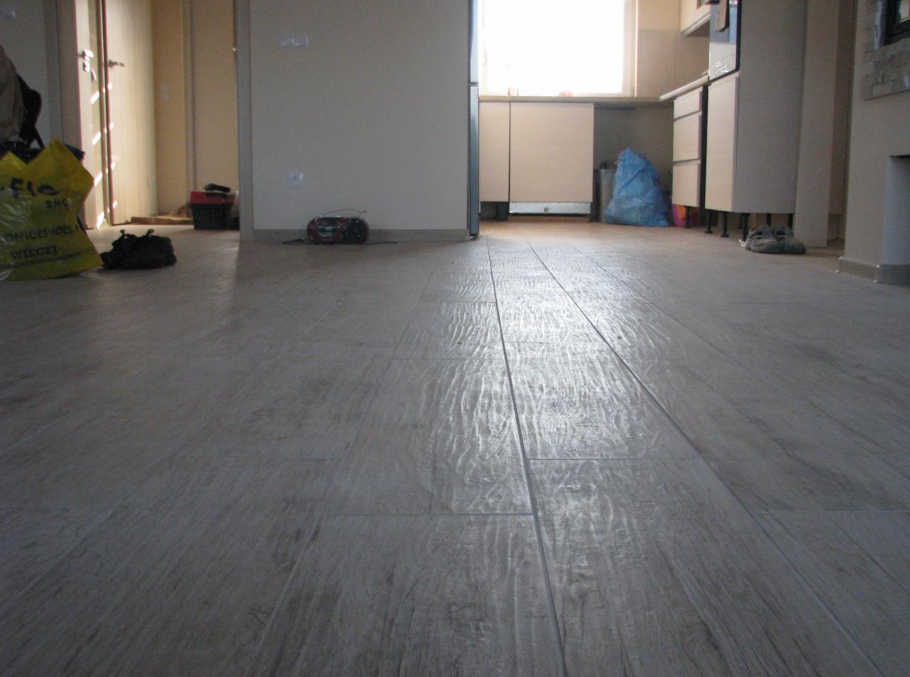 Ułożona podłoga z płytek imitujących drewno, widok z niskiej perspektywy, w tle nieporządek w remontowanym pomieszczeniu.