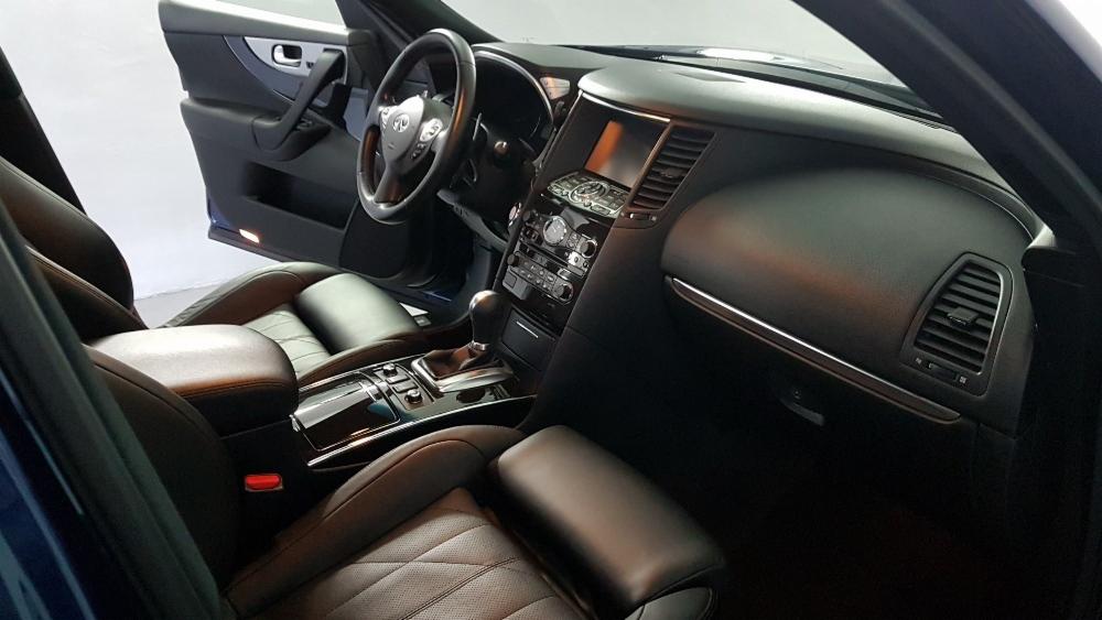 Wnętrze samochodu z czarną skórzaną tapicerką, widoczne fotele, deska rozdzielcza i otwarte drzwi.