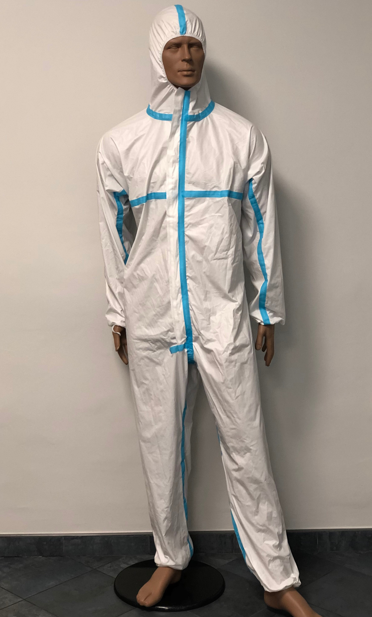 Biały kombinezon ochronny z niebieskimi akcentami, prezentowany na manekinie na tle białej ściany i ciemnej podłogi.