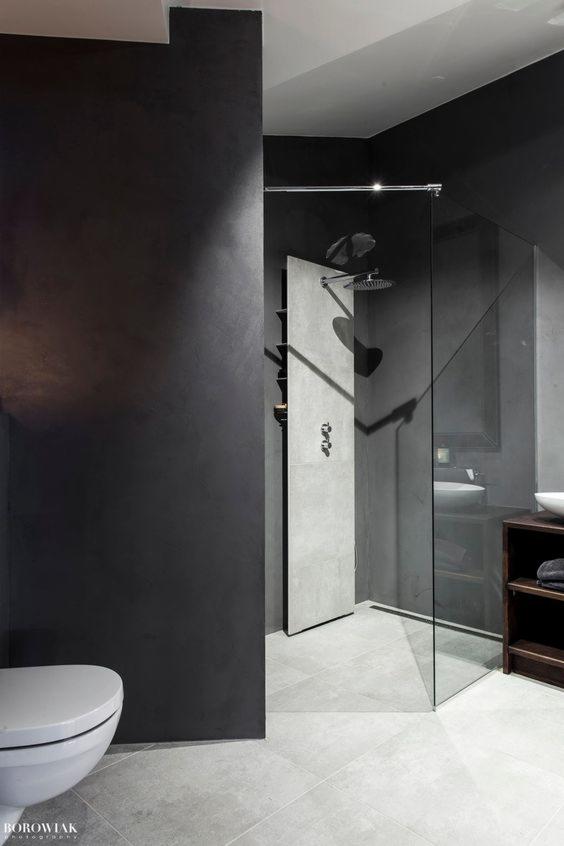 Nowoczesna łazienka w odcieniach szarości z kabiną prysznicową typu walk-in, minimalistyczną armaturą i betonową ścianą, widoczny fragment toalety.