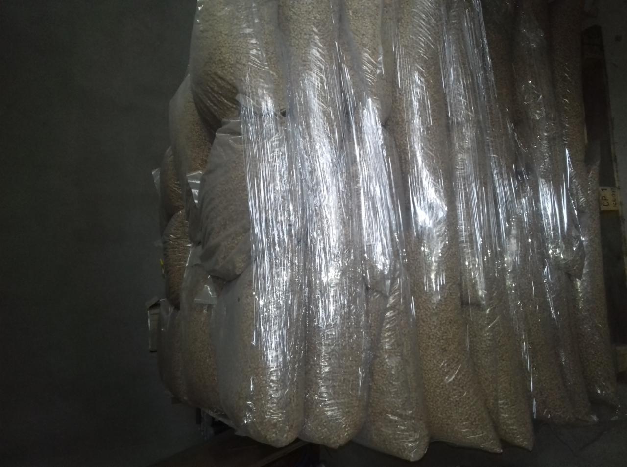 Wielkie worki z granulatem, prawdopodobnie ścierniwem, szczelnie owinięte folią stretch, ustawione w magazynie.