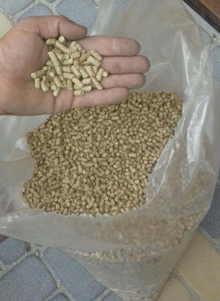 Ręka trzymająca granulki piasku śrutowniczego nad workiem wypełnionym tym samym materiałem, widoczne nierówności i pęknięcia na kilku granulkach.