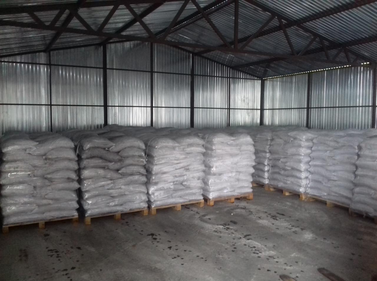 Magazyn z workami na paletach pod blachą falistą, potencjalnie po procesie czyszczenia.