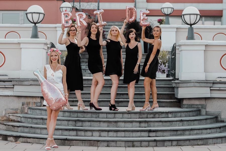 Grupa kobiet świętuje wieczór panieński, trzymając balony z napisem BRIDE na schodach przed budynkiem.