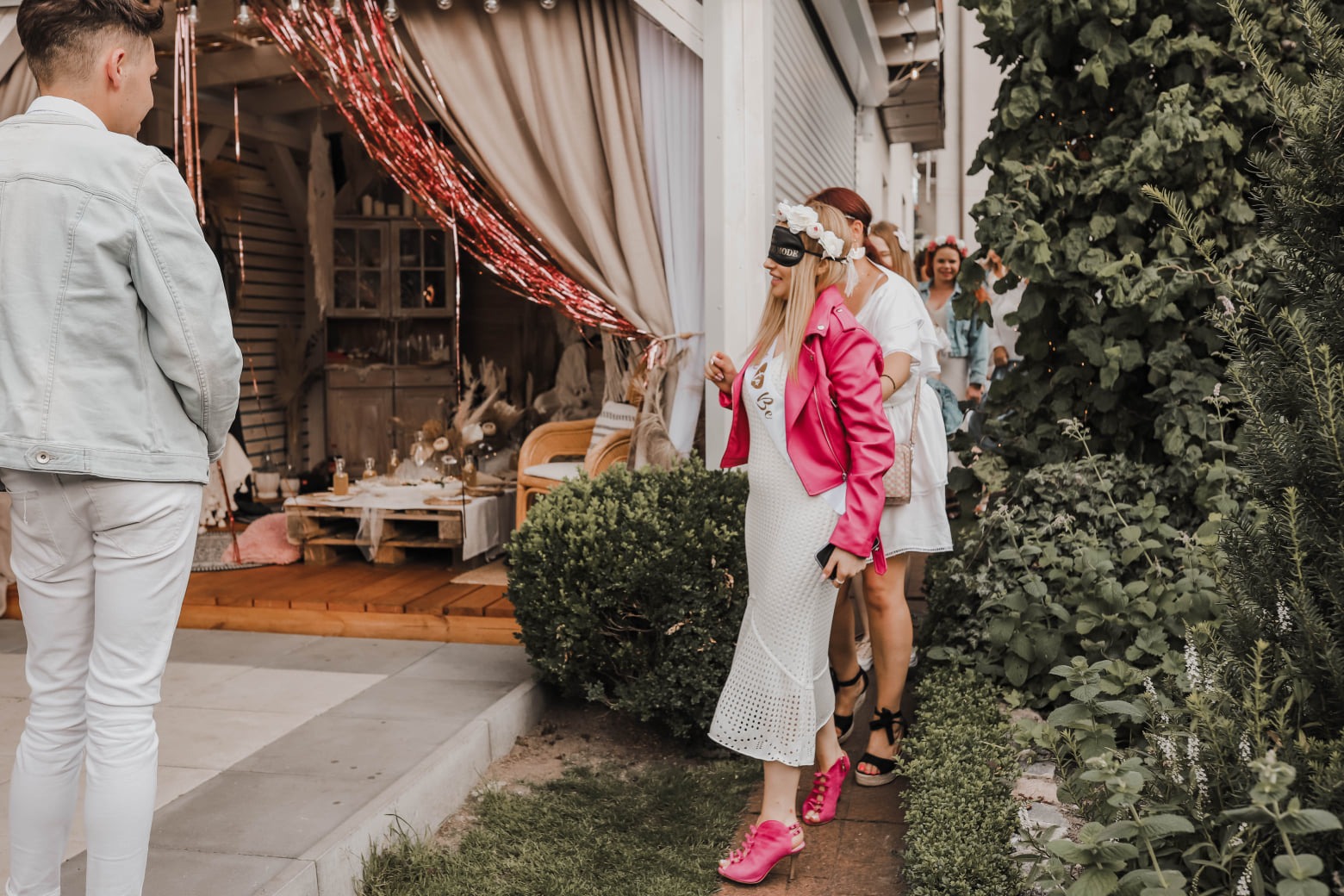 Przyszła panna młoda z zasłoniętymi oczami prowadzona przez gości na przyjęciu z dekoracją w rustykalnym stylu.