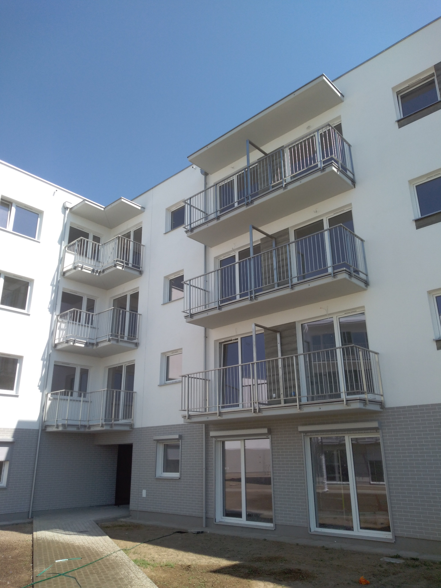 Nowoczesny budynek mieszkalny z balkonami zabezpieczonymi metalowymi balustradami, widok z dołu na elewację z licznymi oknami i niebieskim niebem w tle.