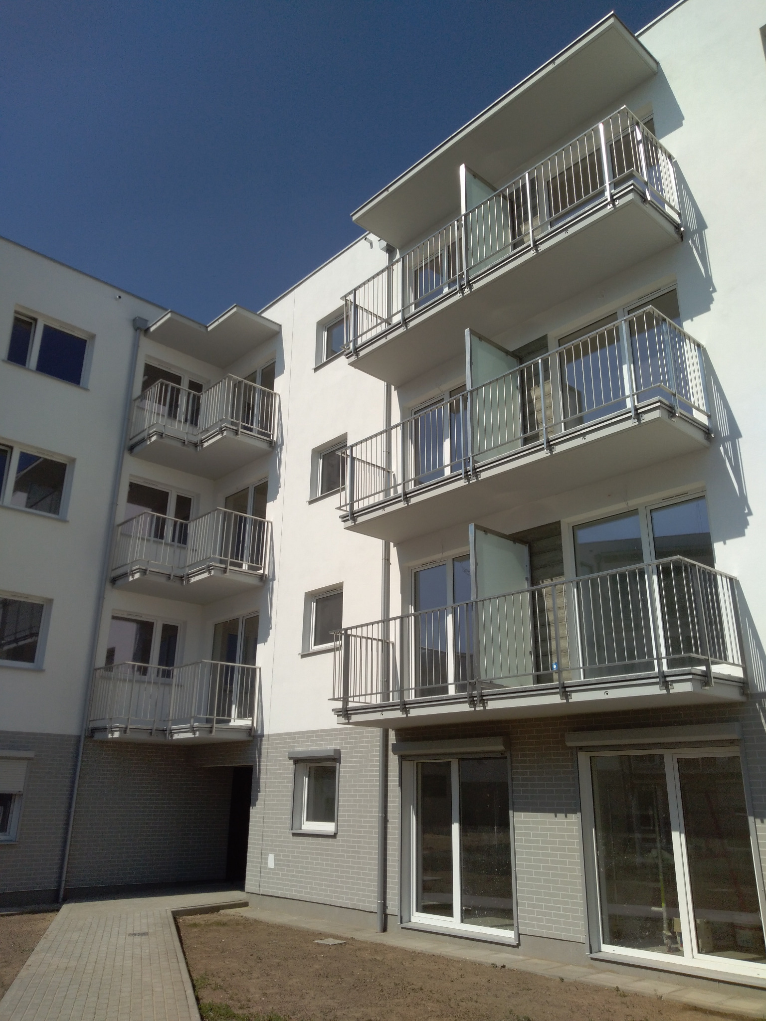 Nowoczesny budynek mieszkalny z balkonami z balustradami nierdzewnymi i szklanymi elementami, widok z dołu na błękitne niebo.