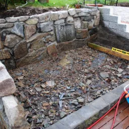 Przygotowanie podłoża pod wylewkę zbrojoną siatką w ogrodzie, widoczny murek z kamienia i poziomica na drewnianej desce.