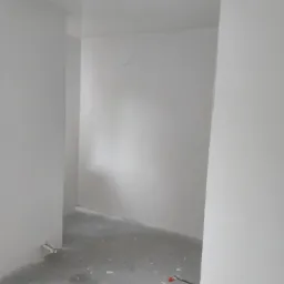 Wnętrze pokoju po pracach przygotowawczych do malowania, z widocznymi śladami szpachli na podłodze i świeżo wygładzonych ścianach, z wystającym kablem ze ściany.