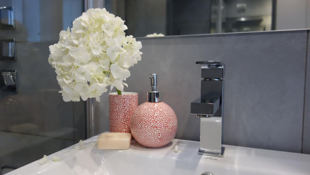 Nowoczesna bateria umywalkowa z hydrangeą w ceramicznym wazonie w kropeczki, obok dozownik do mydła i mydło w kostce na białej umywalce w łazience w Chorzowie.