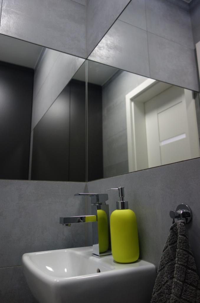 Nowoczesna łazienka z umywalką, chromowaną baterią i żółtym dozownikiem mydła, odbicie w lustrze z szarymi płytkami